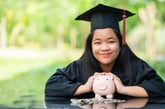 College graduate holds a piggy bank.