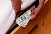 Person hiding cash under bed mattress including several $100 bills in cash