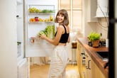 Happy woman smiling in the kitchen looking in the fridge picking up lettuce or a healthy vegetable