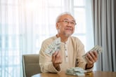 Senior man smiling and holding wads of cash money for retirement