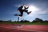 A businessman jumps over a hurdle.