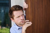 Worried man spying around a door