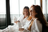 Two women drinking coffee in a hotel room.