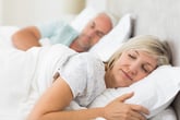 An older couple sleep in a bed