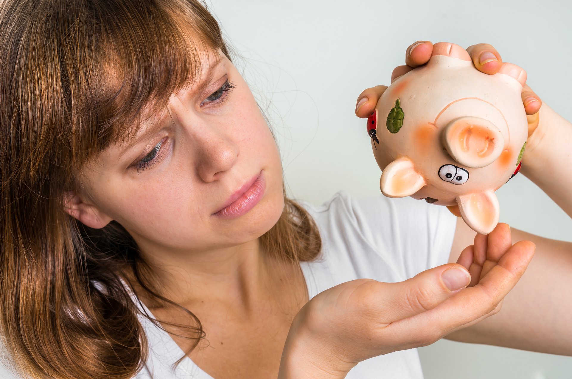 A woman holds a piggy bank upside down