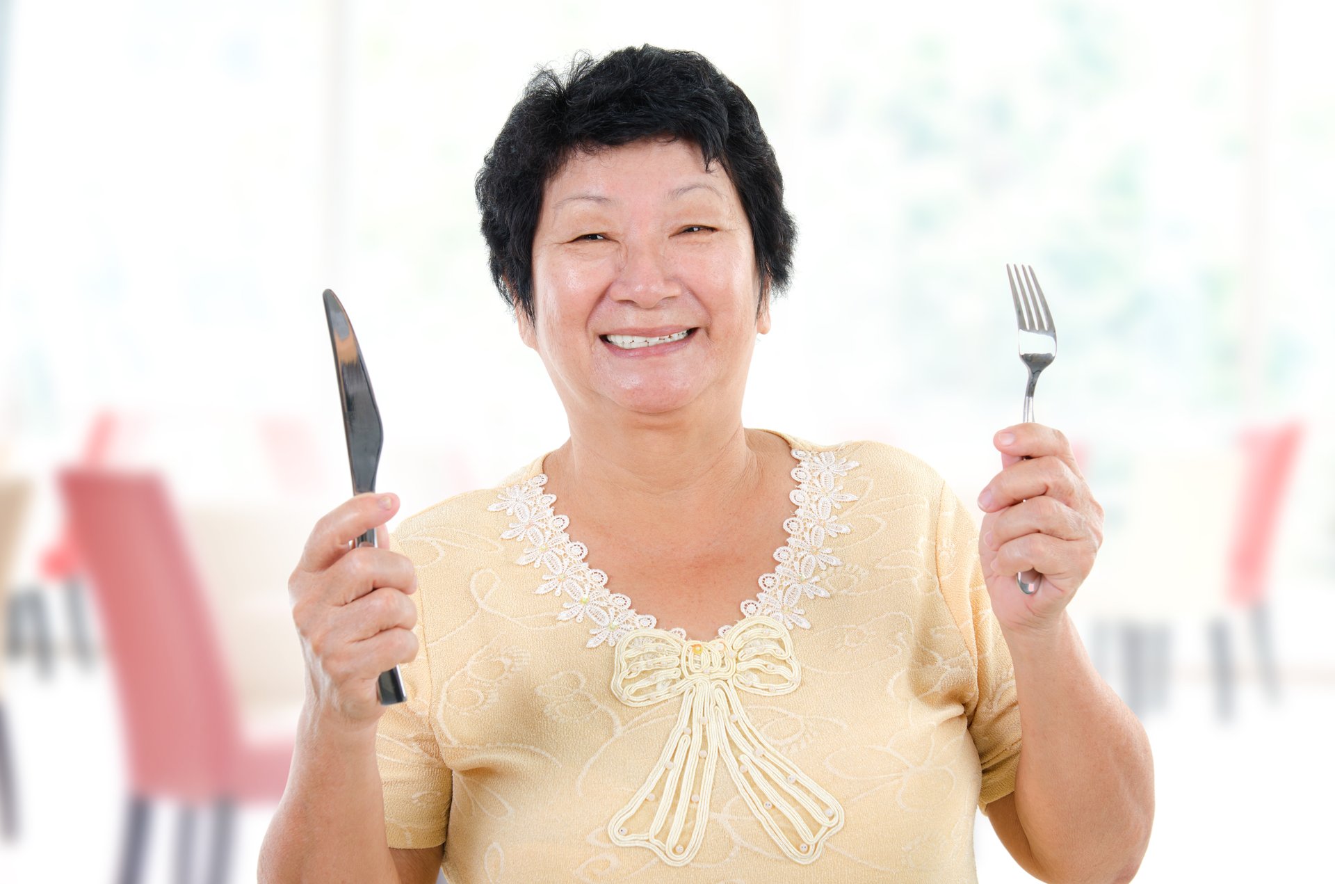 A senior Asian woman holds up a knife and fork at a restaurant