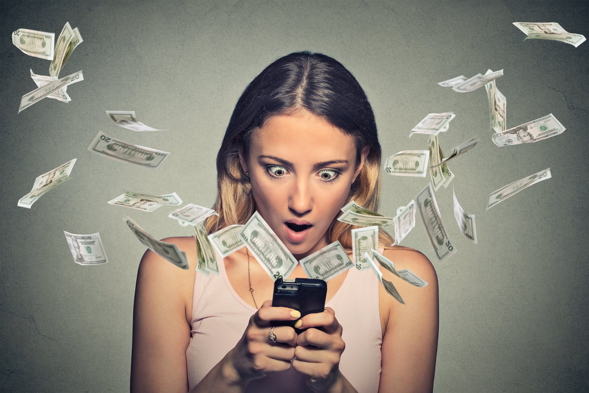 Shocked-looking woman staring at dollar bills flying out of her cellphone.