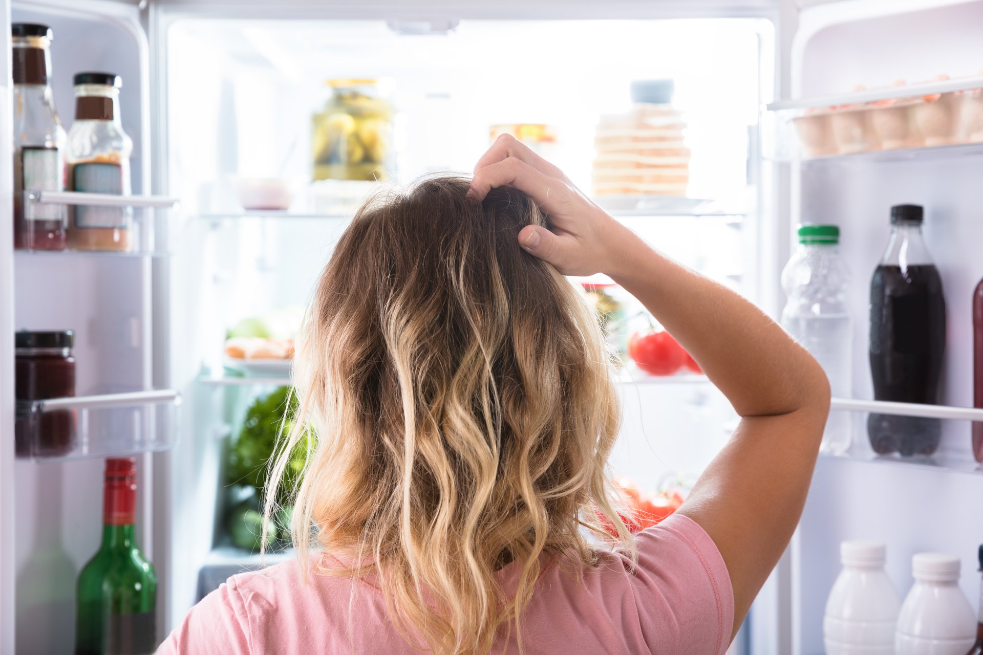 woman scratches her head while staring into her refrigerator