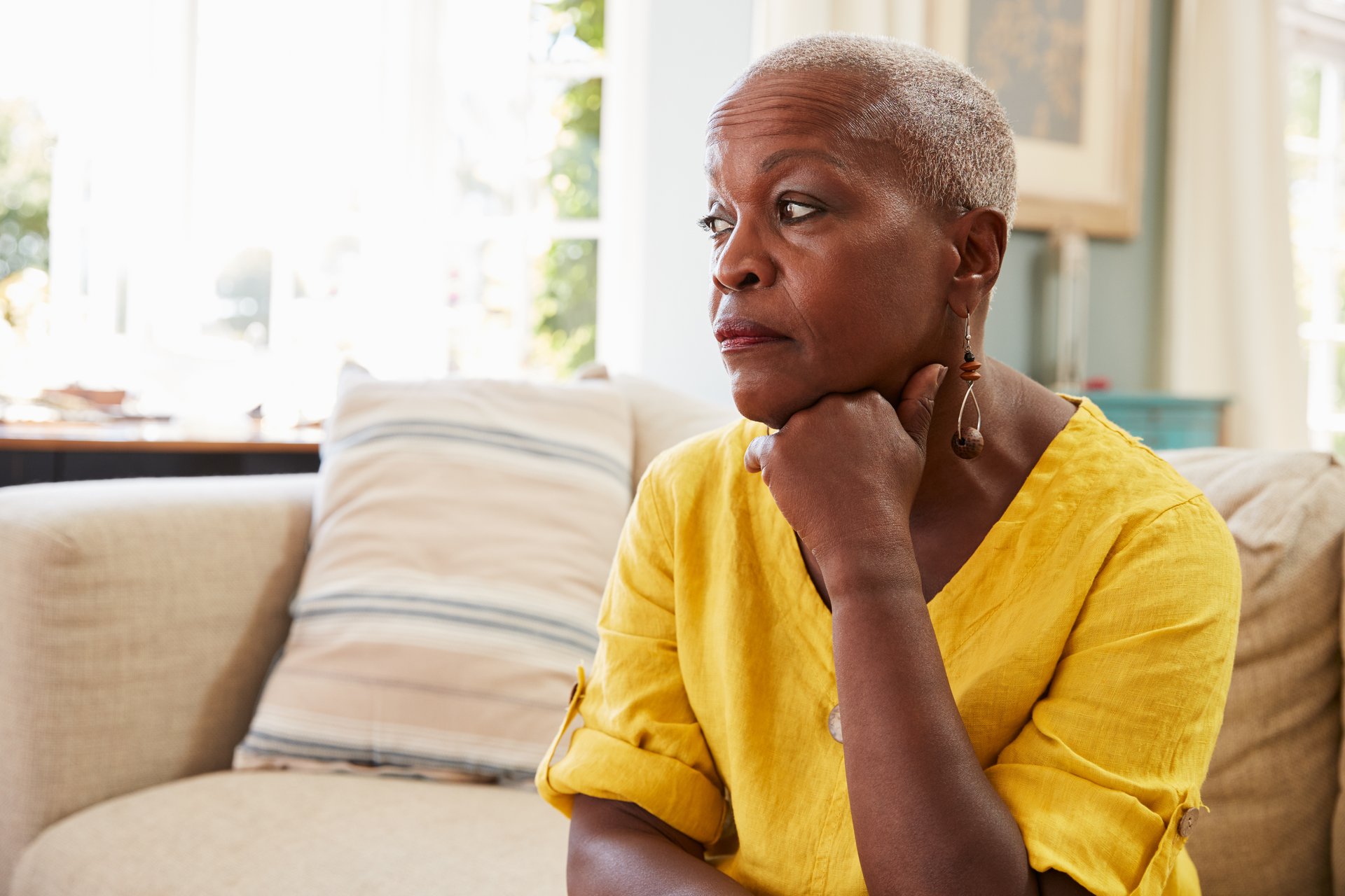 A worried senior black woman sits on her couch