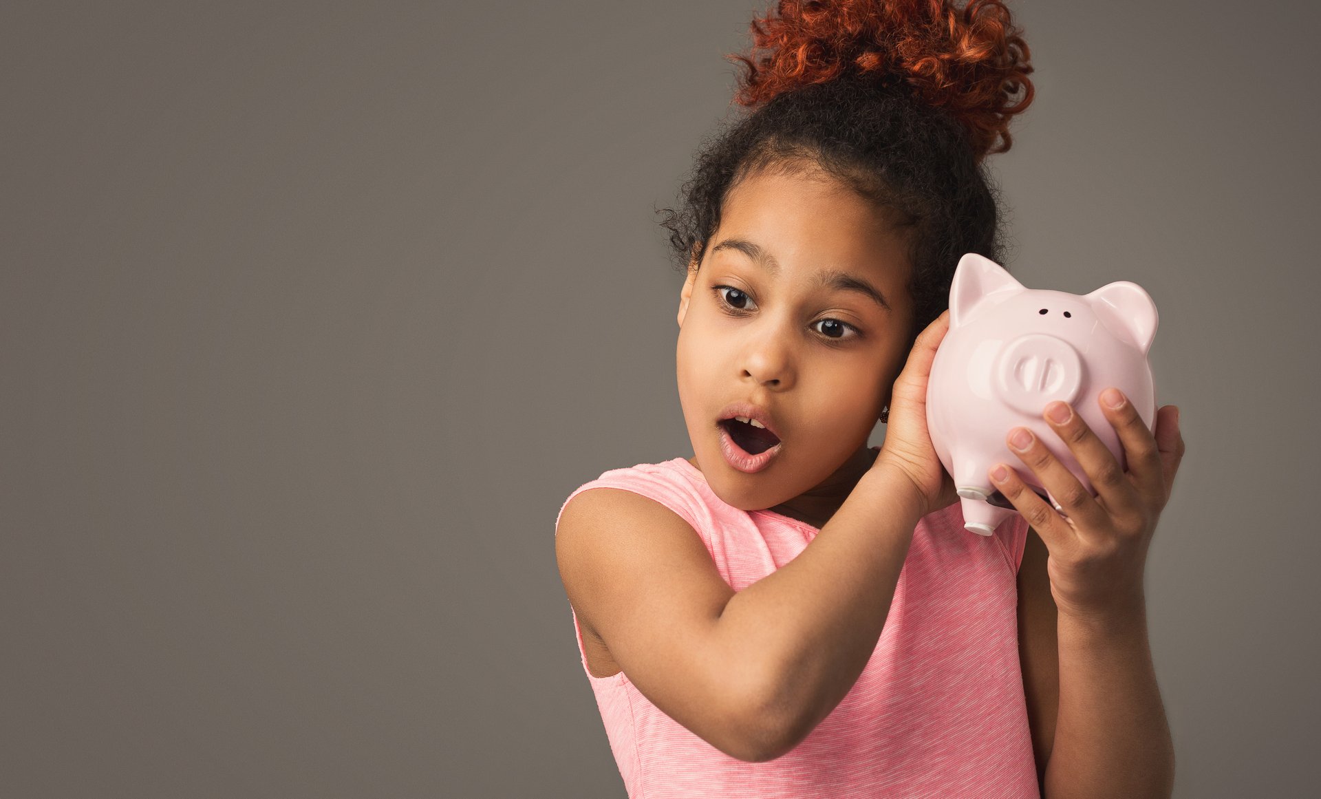A little girl holds a piggy bank up to her ear