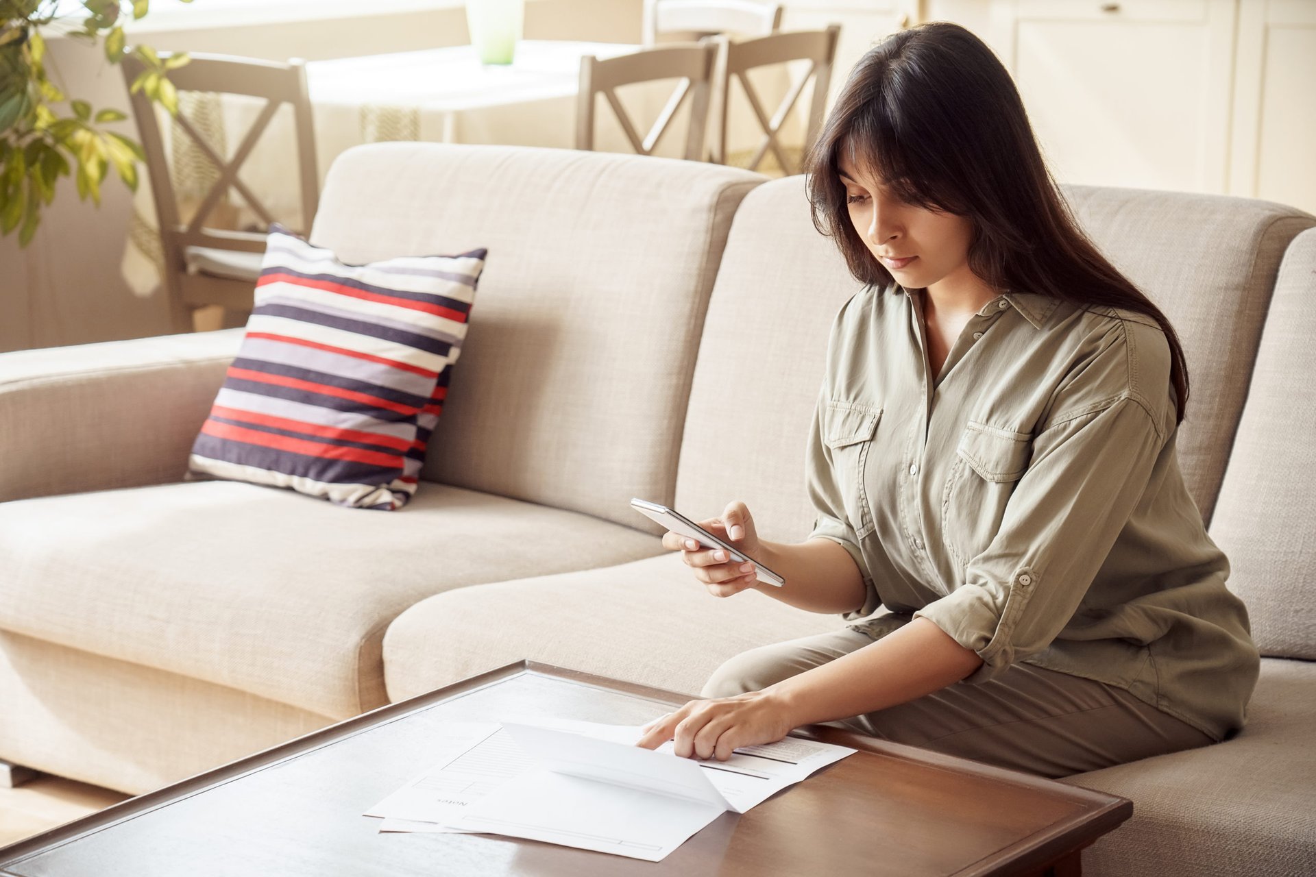 Woman checking her investments on phone and paper statement