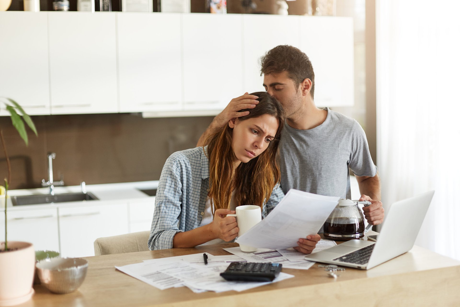 Worried couple looking at bills in the morning at home with laptop and coffee