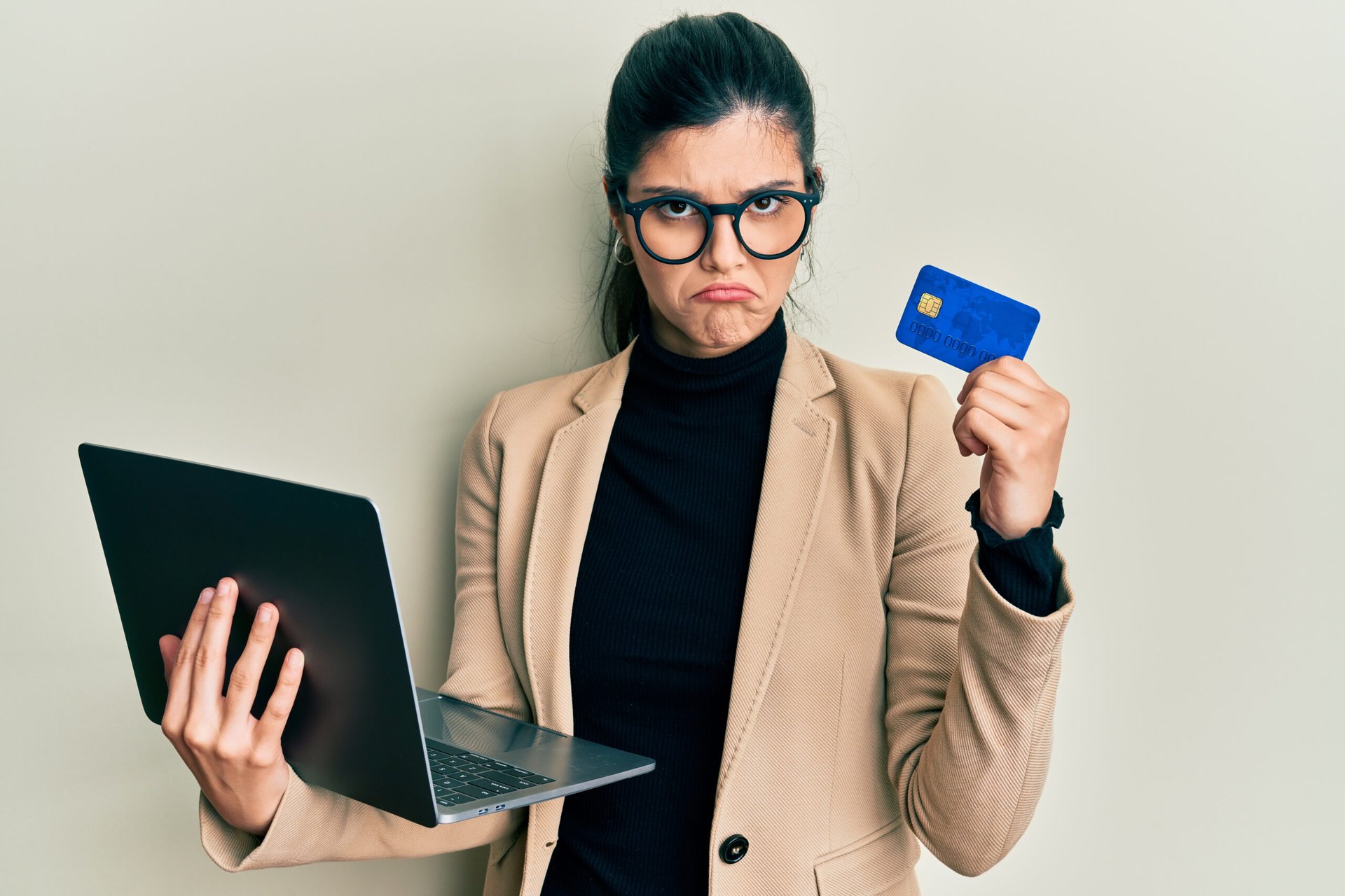Upset woman holding a credit card and laptop
