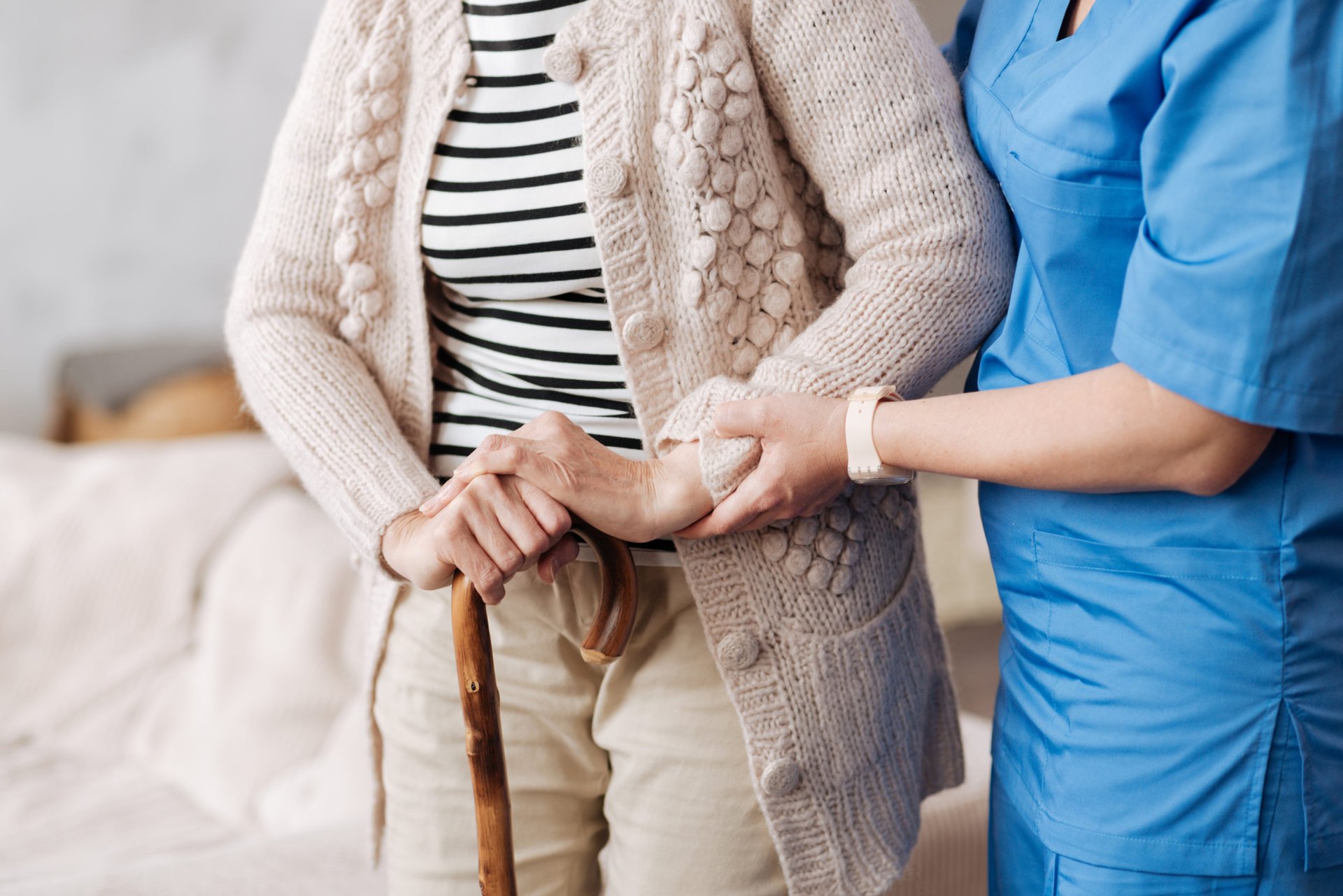 A nurse helps an older patient walk with a cane