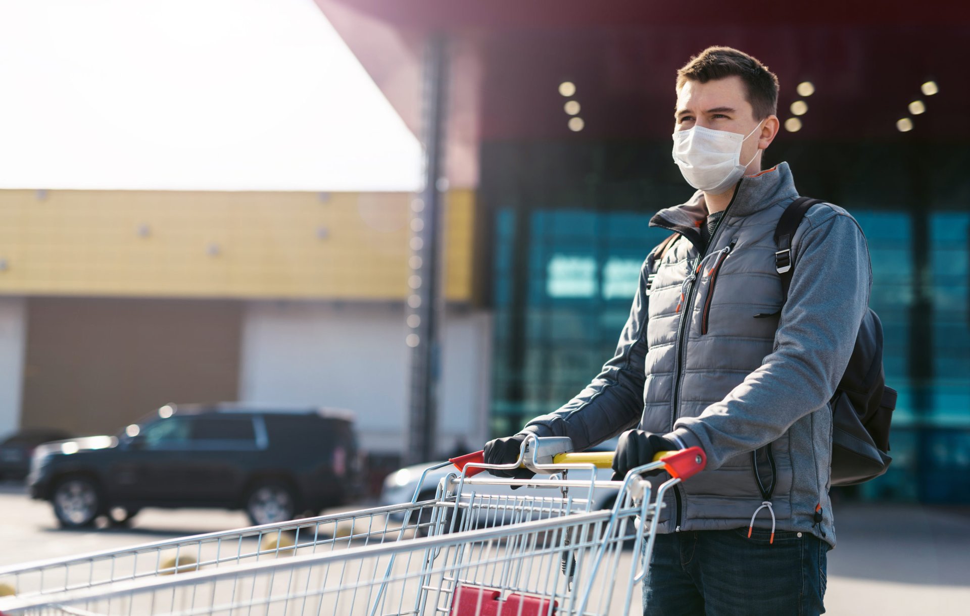 A shopper in a mask pushes a cart outside a store