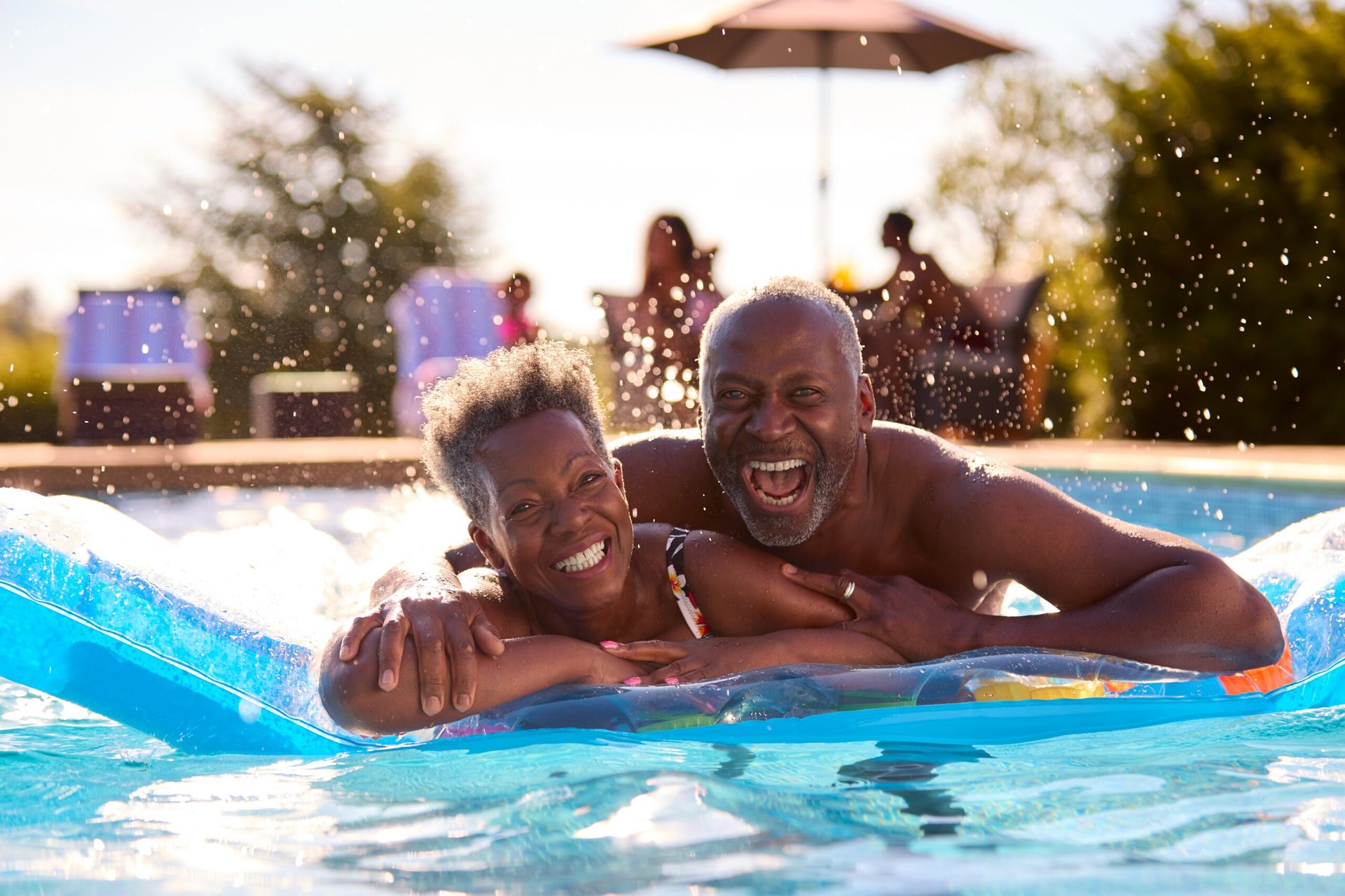 Happy senior couple grinning and swimming at the pool on vacation or at a hotel with a pool float raft