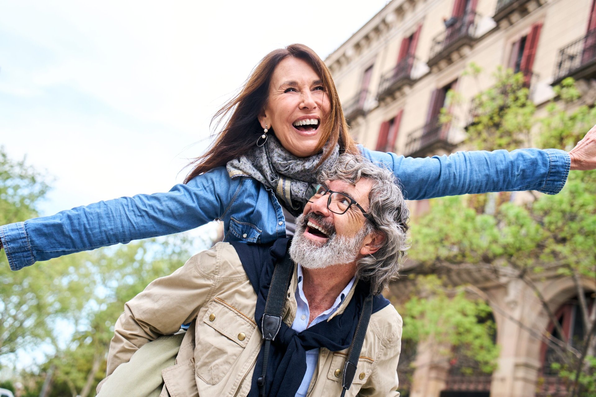 Happy senior couple outdoors in the city with a man carrying a woman piggyback and laughing