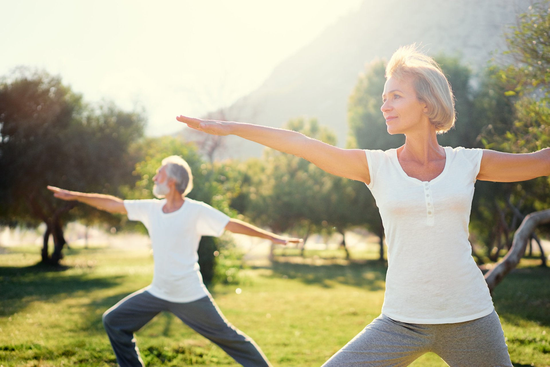 Happy relaxed seniors doing yoga outdoors in a sunny area during retirement