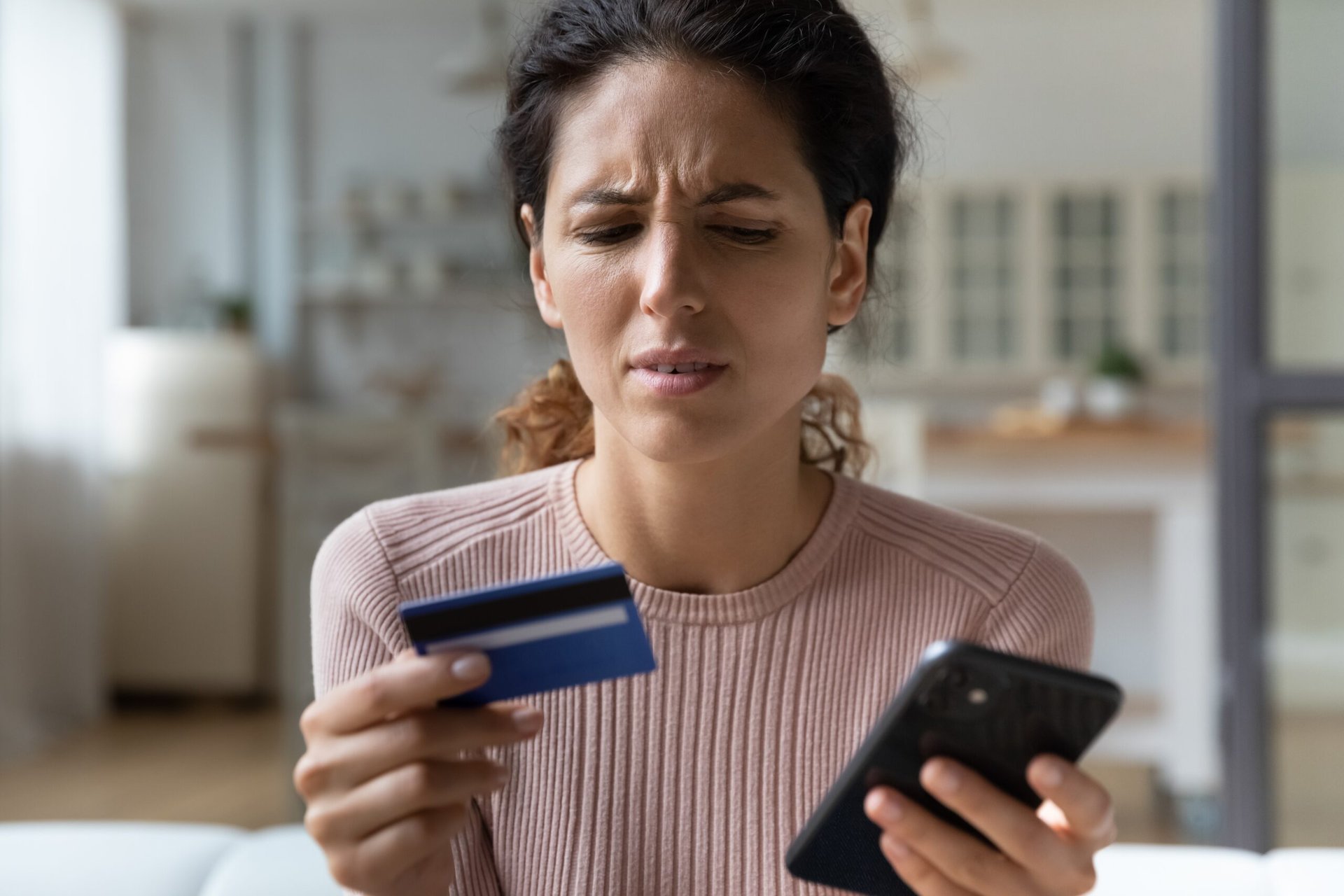Woman looking at her phone skeptical or sad while holding credit card