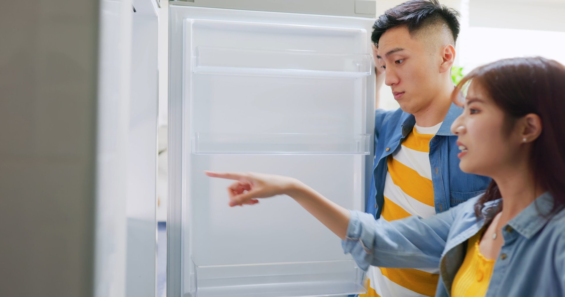 Asian couple pointing in fridge and looking for food