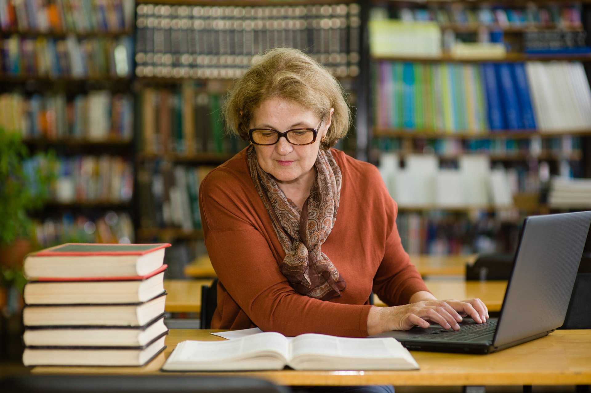 Older woman student using laptop in library studying