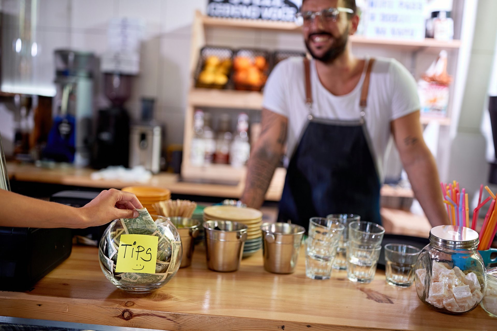Smiling employee watching money go in the tip jar at the coffee shop