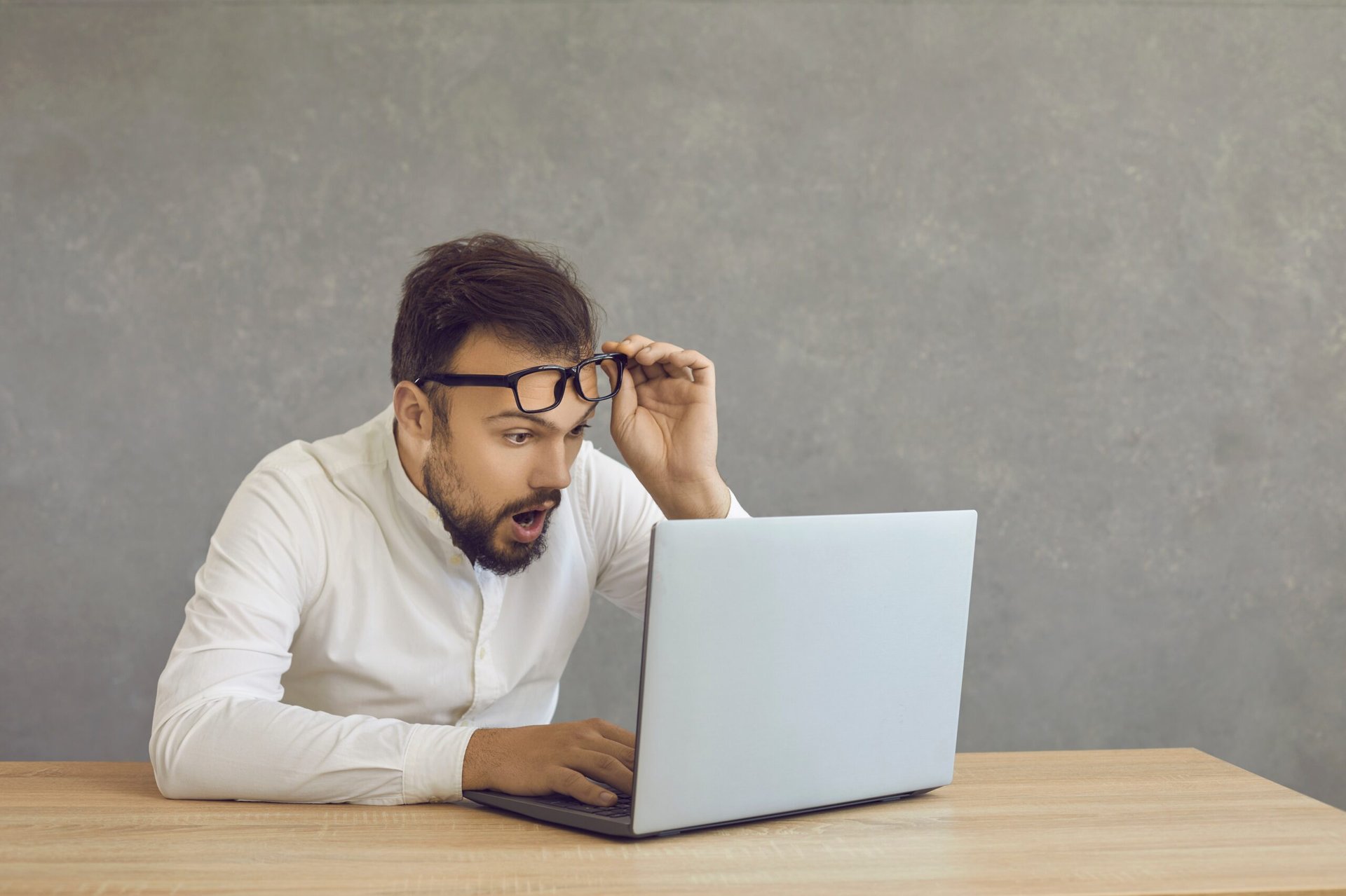 Employé ou homme d'affaires stupéfait utilisant un ordinateur portable à distance enlevant des lunettes de surprise
