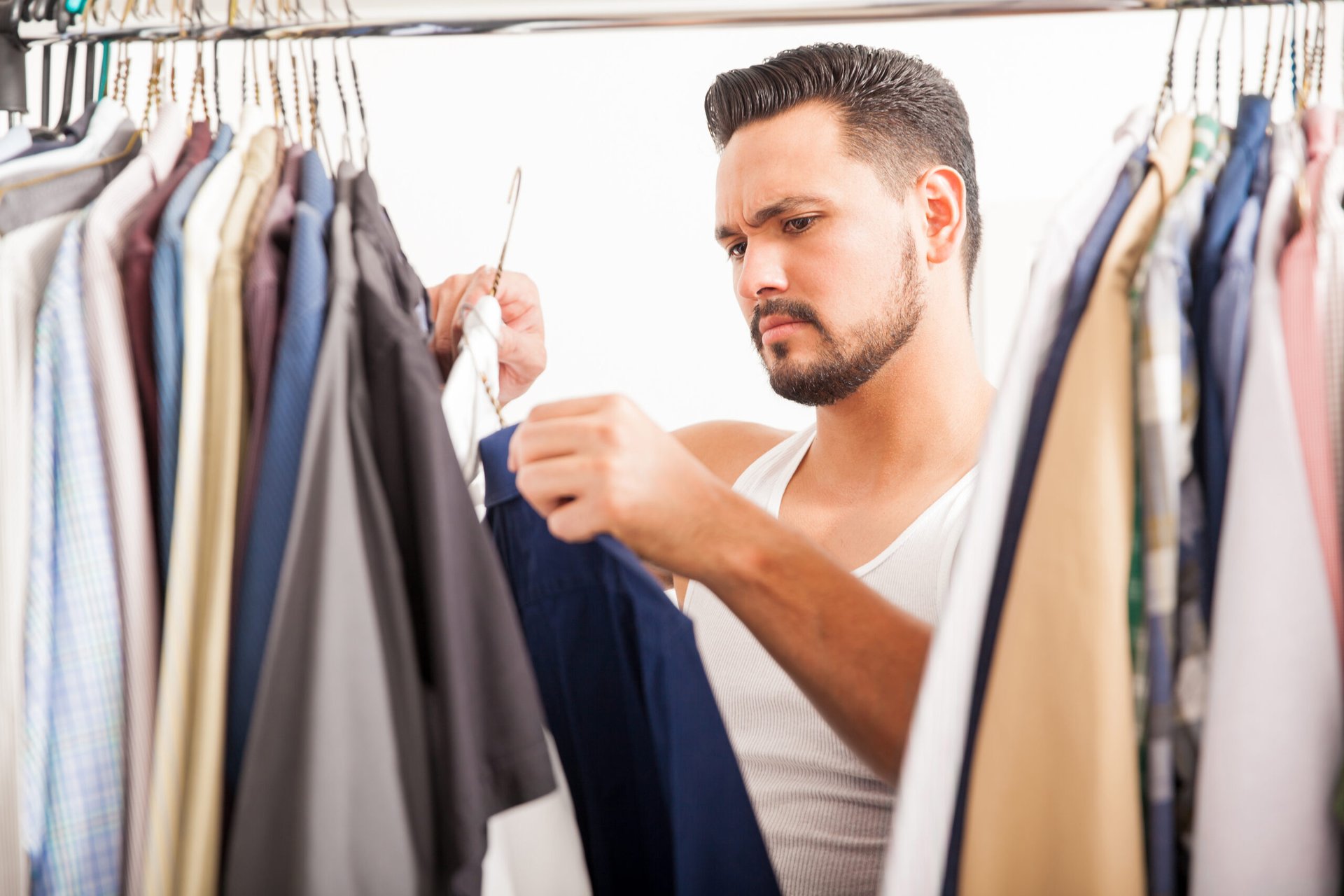 young man choosing between to shirts to wear while looking through his closet