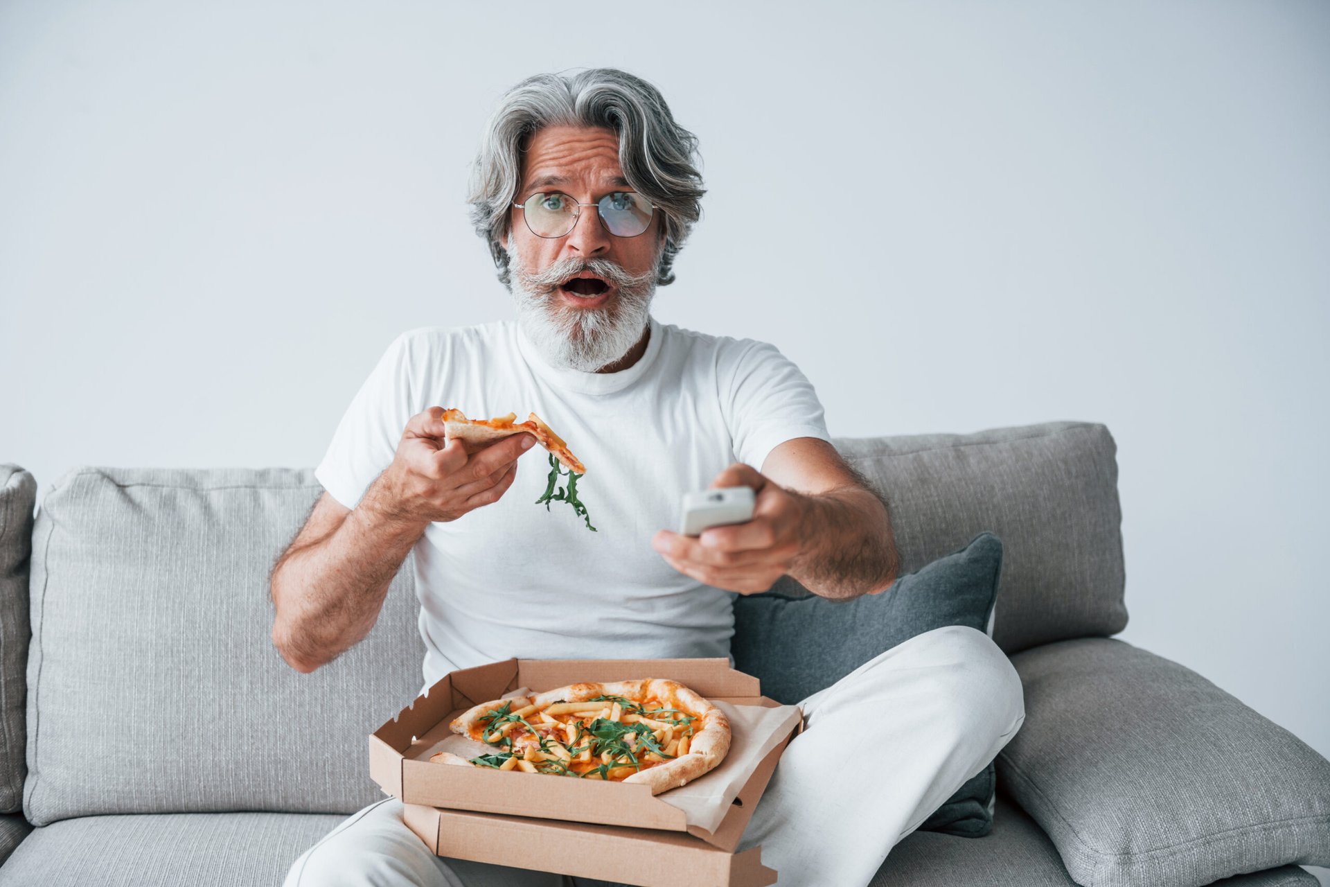 Senior man watching TV and eating pizza