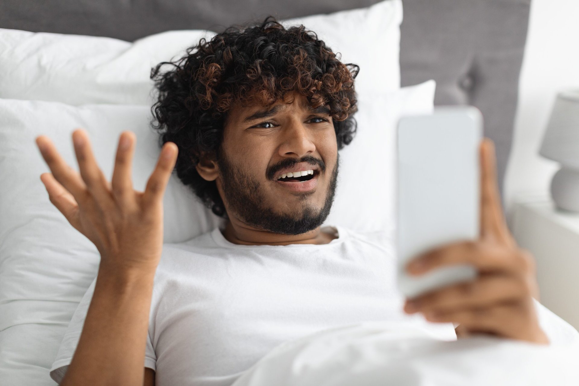 Confused or frustrated man lying in bed looking at weird message on his phone
