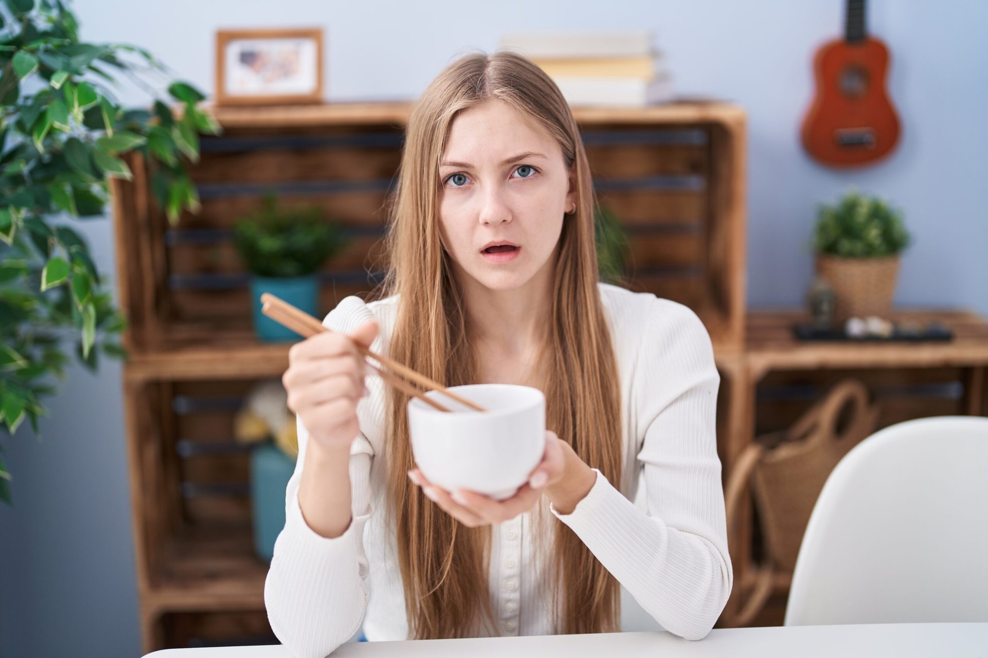 Upset woman eating food out of a bowl with chopsticks.