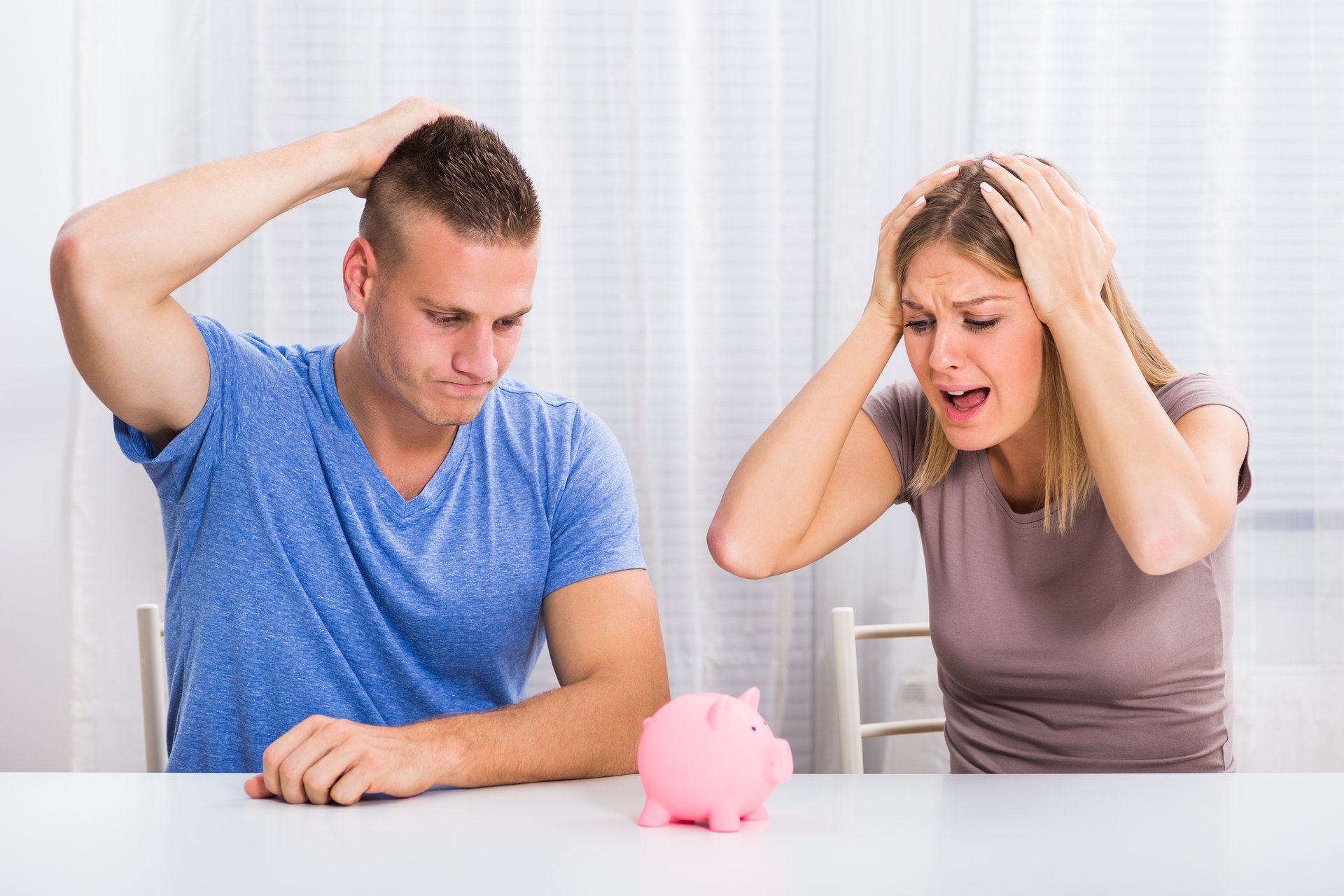 Couple tearing their hair, looking at a piggy bank.