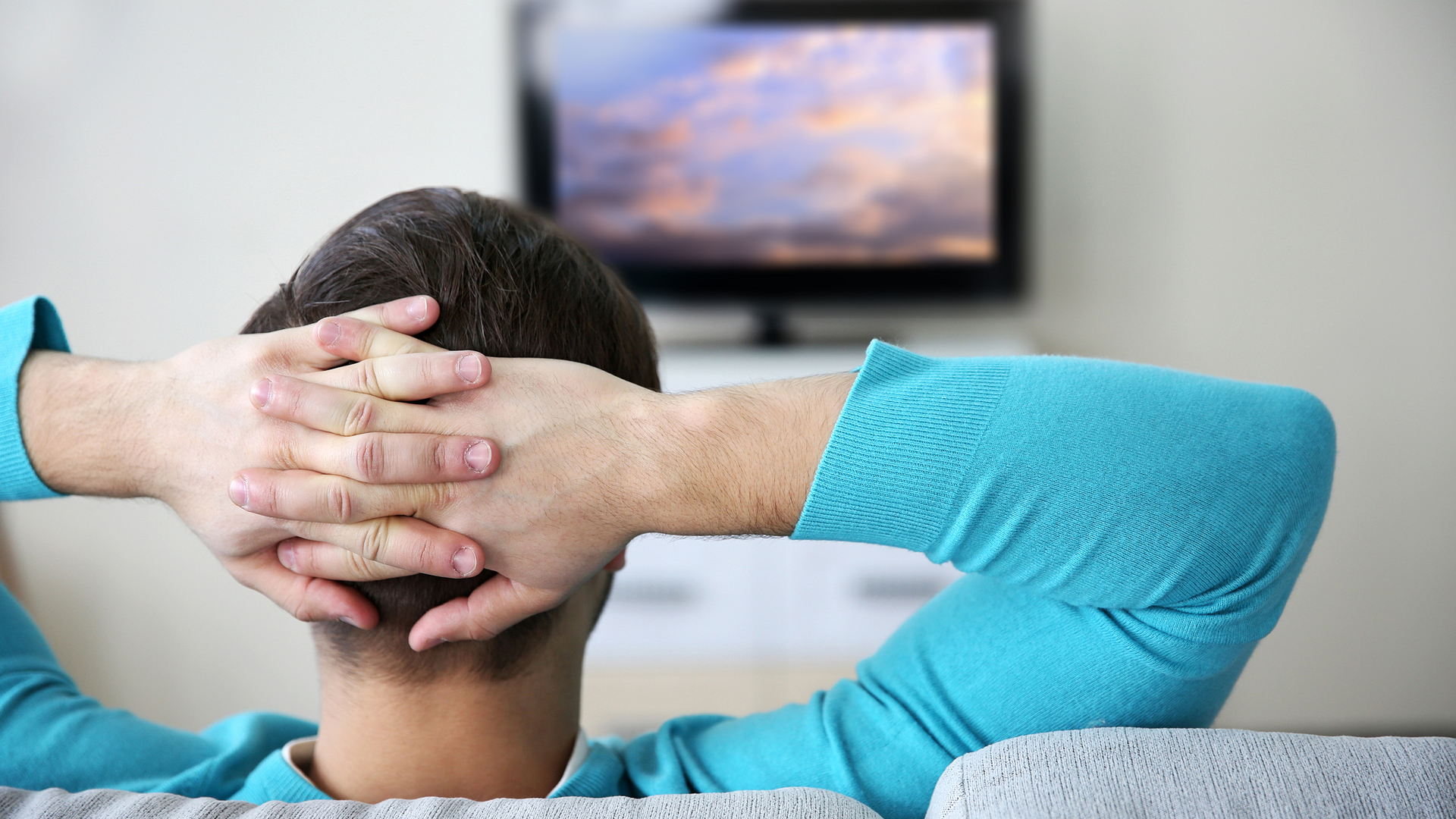 A relaxed man watches video on a flat-screen TV