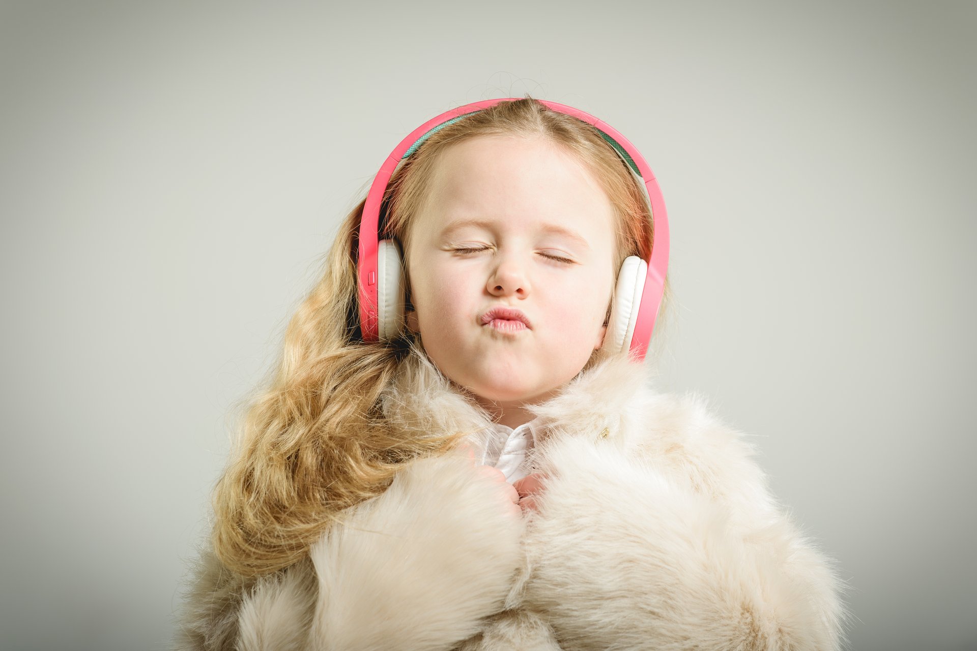 A young girl listens to music on pink headphones