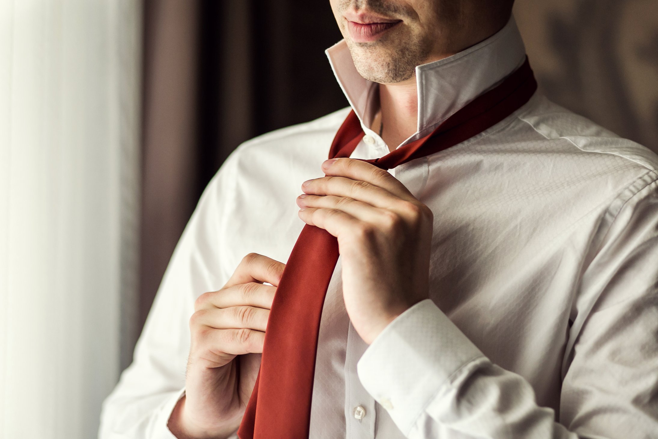 Man in white shirt putting on a tie. bondvit / Shutterstock.com. 