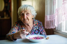 Senior woman eating soup or messy pie in a bowl by the kitchen window