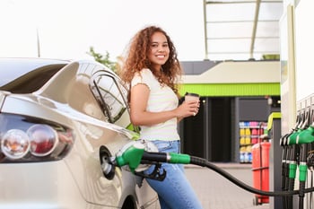 Happy woman pumping gas at the gas station with a fuel discount