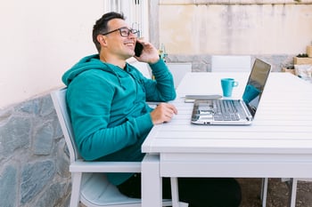 Happy remote worker talking on the phone while working on laptop