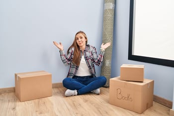 Homebuyer or renter shrugging with a pile of packed boxes ready to move to a new home from empty house