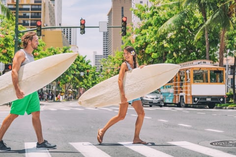 Happy surfers walking across the street with surfboards headed to the beach in Honolulu, Hawaii