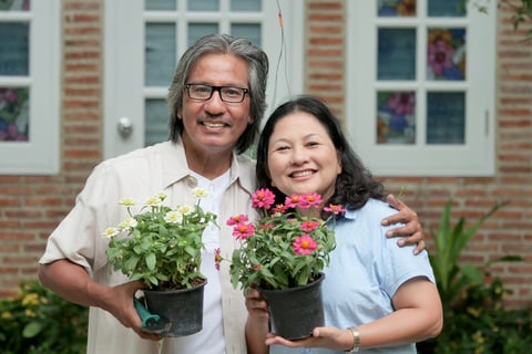 A couple holds flower pots in front of their home