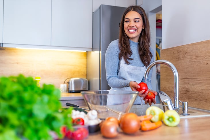 A woman washes produce in a kitchen sink