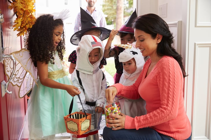A woman hands out candy to young children in costume