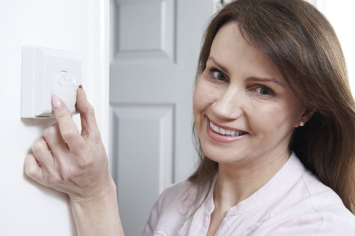 A woman adjusts a thermostat