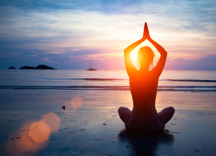A woman practices yoga on the beach at sunset