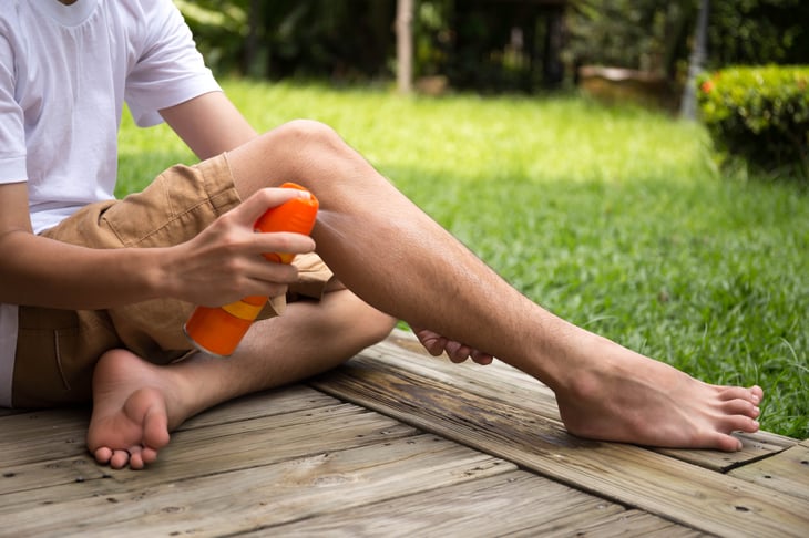 A boy sprays his legs with insect repellent while outdoors