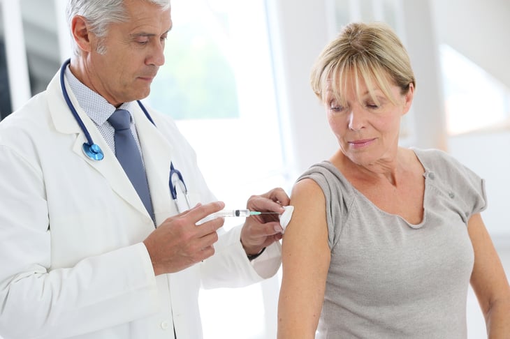 A medical doctor in a white lab coat injects a needle into an older woman