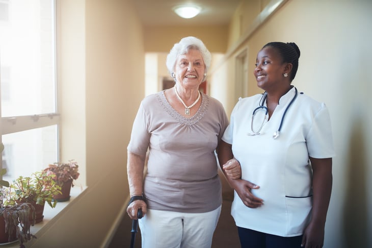 Elderly woman walking with homecare worker in white smock