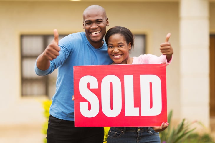 A couple holds a "Sold" sign in front of their home