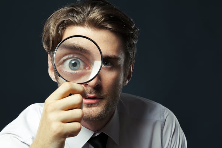 A man holds up and looks through a magnifying glass